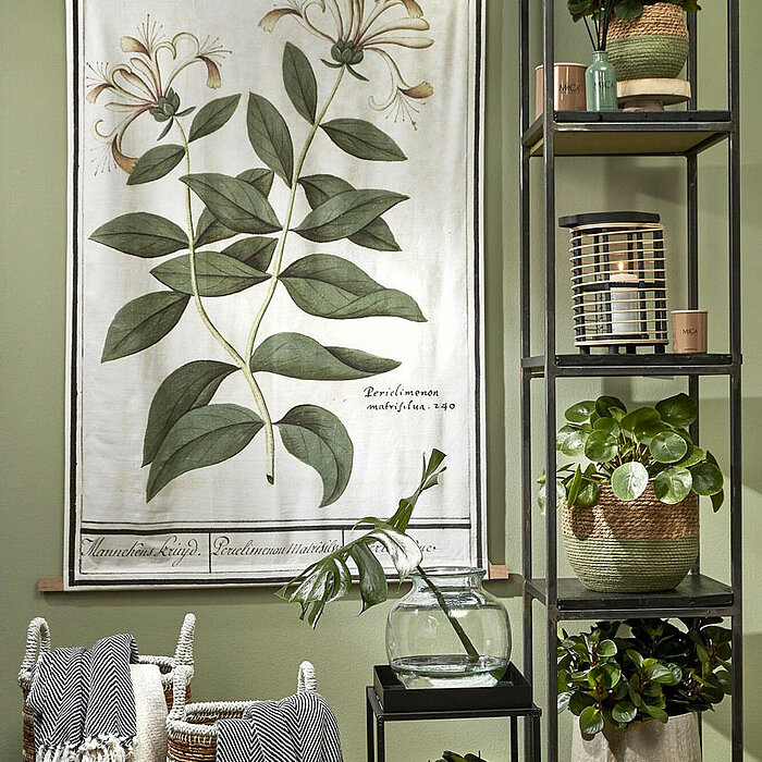 Das Bild zeigt eine Nahaufnahme einer Decke mit einem markanten, zickzackförmigen Muster in dunklem Grün und Weiß. Im linken Teil des Bildes sind weiße Fransen am Rand der Decke zu sehen. Der rechte Teil des Bildes zeigt ein Etikett mit der Aufschrift "Mo