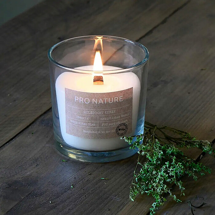 Sechs brennende Kerzen des Herstellers Müller in verschiedenen Formen und Größen auf einem Holztisch. Es gibt vier weiße Stumpenkerzen in verschiedenen Höhen, drei Teelichtkerzen in klaren Glasbehältern und zwei hohe, weiße Stabkerzen. Auf dem Tisch befin