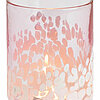 Eine einzelne brennende Kerze in einem rosa und weiß gesprenkelten Glasgefäß. Das Glas hat eine zylindrische Form und das Licht der Flamme strahlt sanft durch die rosa-weißen Muster, die an Wolken oder Blütenblätter erinnern. Die Farben und das sanfte Leu