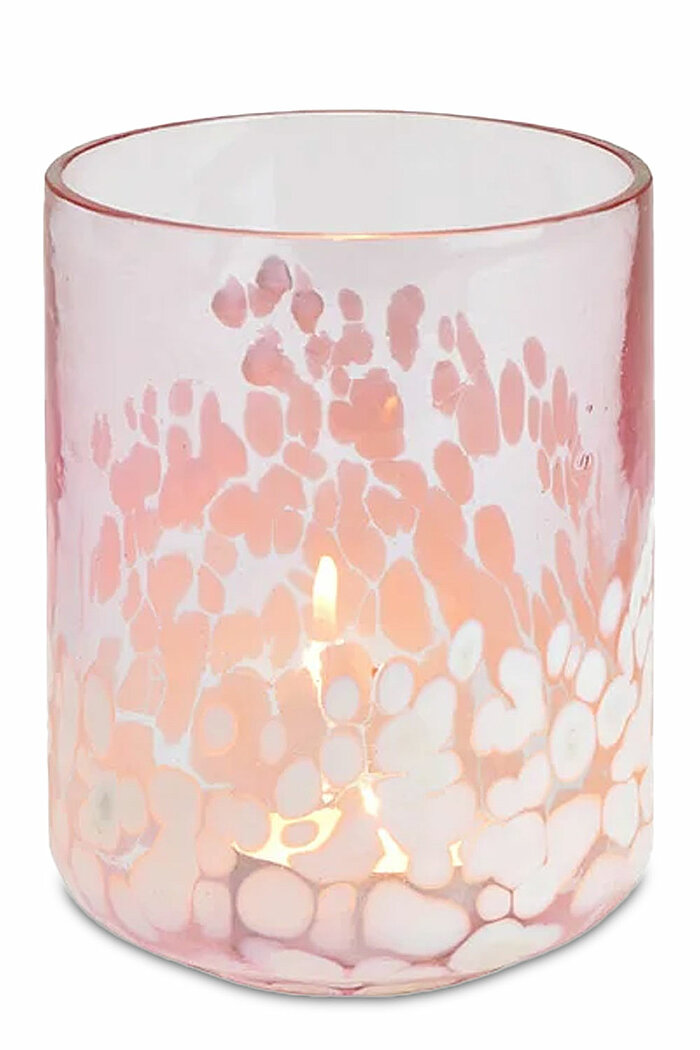 Eine einzelne brennende Kerze in einem rosa und weiß gesprenkelten Glasgefäß. Das Glas hat eine zylindrische Form und das Licht der Flamme strahlt sanft durch die rosa-weißen Muster, die an Wolken oder Blütenblätter erinnern. Die Farben und das sanfte Leu