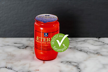 Auf dem Bild steht auf einem armorierten Boden eine Aeterna Grabkerze in rot. Es ist ein grüner Kerzenprofi getestet Button zu sehen. Der Hintergrund ist in einem ruhigen grauen Ton ohne Dekoration