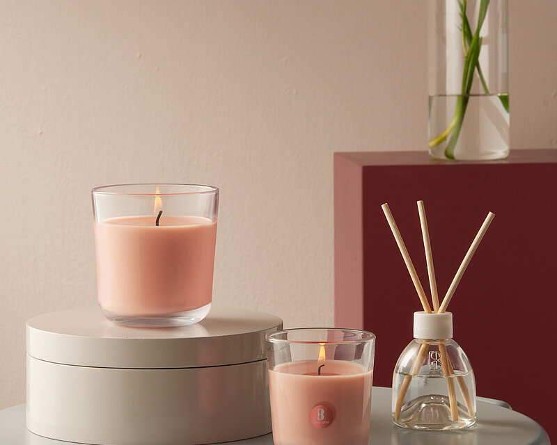 Heller, gemütlicher Raum mit einem kleinen Tisch im Vordergrund. Auf dem Tisch stehen zwei pfirsichfarbene Duftgläser, daneben ein Raumduft-Diffuser mit Rattanstäbchen.