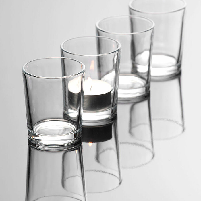 Drei brennende Teelichter in klaren und mattierten Glasbehältern vom Hersteller "Sandra Rich" stehen auf einem runden, schwarzen Tablett mit Griffen. Die schlichten, eleganten Teelichter schaffen eine gemütliche Atmosphäre.