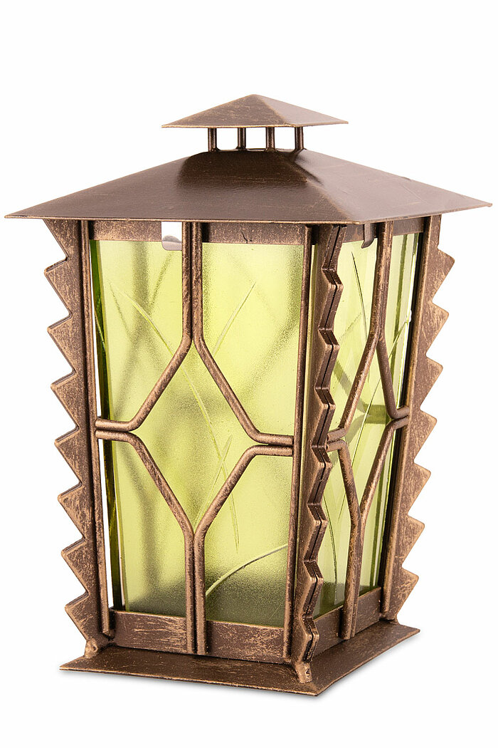 Eine dekorative, bronzefarbene Laterne mit einem spitzen Dach. Die Seiten sind mit transparenten, grünen Scheiben versehen, die ein feines, eingraviertes Muster zeigen. Die Kanten der Laterne sind mit gezackten Metallakzenten verziert, die dem Design zusä