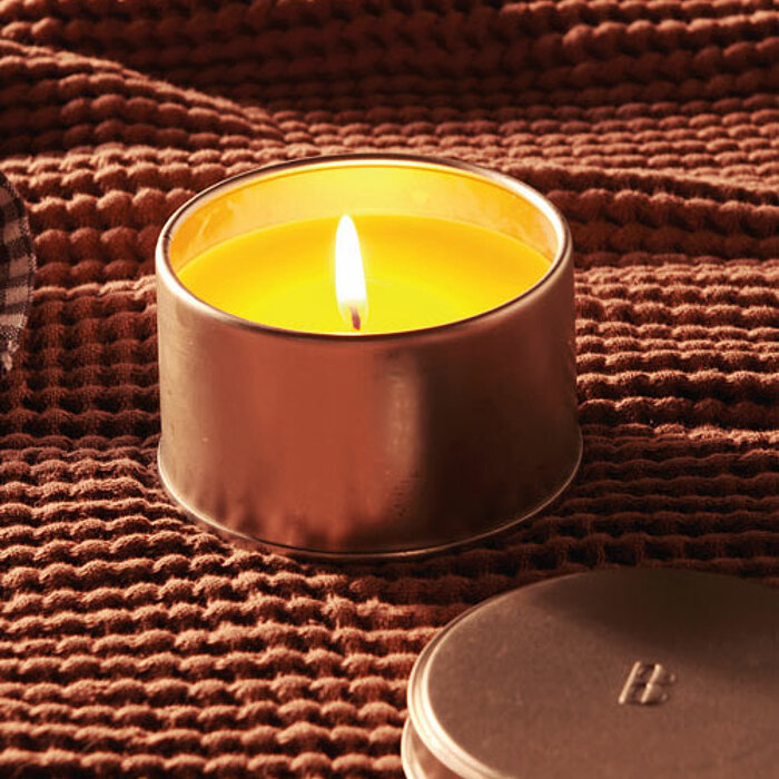 Mehrere brennende Windlichter von Bolsius in verschiedenen Farben und Größen schmücken einen rustikalen Holztisch. Zwischen den Windlichtern stehen Wasser- und Weingläser sowie dunkelgraue Teller, die auf eine gemütliche, einladende Stimmung hinweisen.