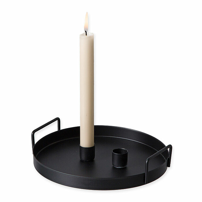 Eine brennende, schmale, cremefarbene Stabkerze vom Hersteller "Halbach" steht auf einem schwarzen Metalltablett mit hohen Kanten und zwei Griffen. Hinter der brennenden Kerze befindet sich ein zusätzlicher leerer Kerzenhalter. Das Bild strahlt eine schli
