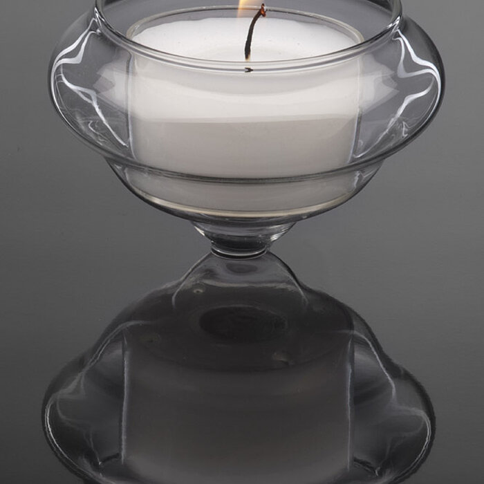 Eine brennende Teelichtkerze vom Hersteller "Sandra Rich" ist in einem eleganten, transparenten Glasbehälter platziert. Der Glasbehälter hat eine geschwungene Form, die die Flamme dramatisch und schön reflektiert. Der dunkle Hintergrund hebt die sanfte Be