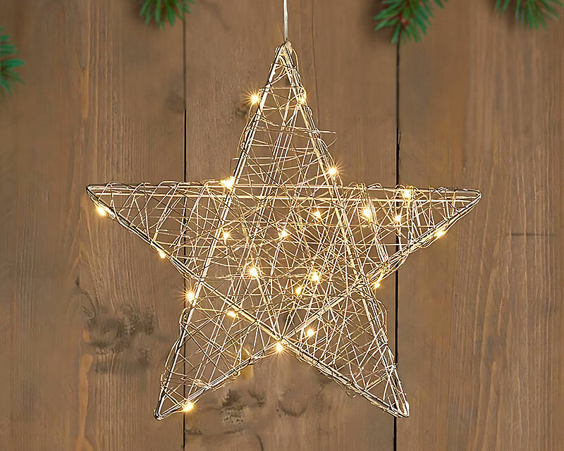 Ein schöner LED-Drahtstern, der warmes Licht ausstrahlt, hängt von oben herab. Im Hintergrund ist eine mit Tannenzweigen weihnachtlich geschmückte Wand zu erkennen, die eine festliche und gemütliche Stimmung verbreitet