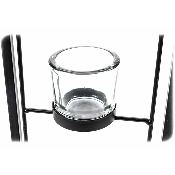 Ein leerer, transparenter Glaskerzenhalter ist in einer schwarzen Metallhalterung platziert. Der Halter hat eine zylindrische Form und wird von zwei horizontalen Metallstangen getragen. Die Metallhalterung besteht aus dünnen Streben, die einen klaren, min