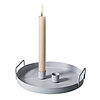 Eine brennende Stabkerze von Halbach in einem hellen Kerzenhalter, der auf einem runden silberfarbenen Tablett mit Griffen steht. Das schlichte, minimalistische Design des Kerzenhalters und Tabletts vermittelt eine ruhige und moderne Stimmung.