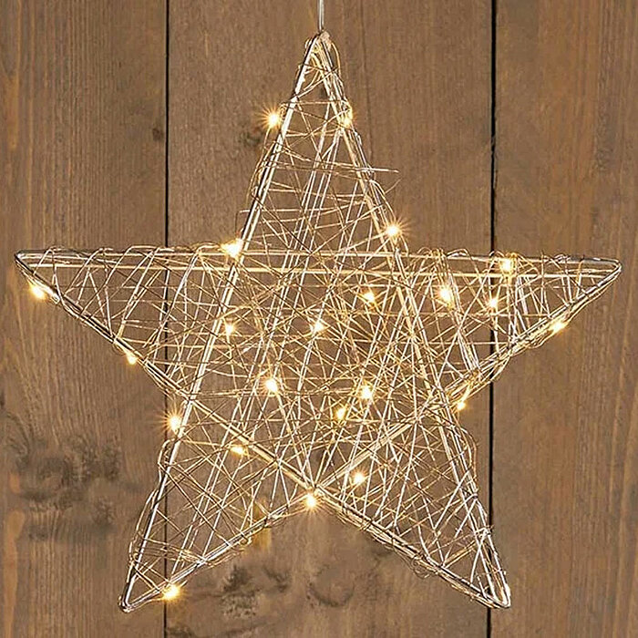 Ein leuchtender Stern aus filigranem Drahtgeflecht, der mit kleinen warmweißen Lichtern durchzogen ist, hängt vor einer rustikalen Holzwand. Die Lichter verleihen dem Stern eine gemütliche und festliche Ausstrahlung.