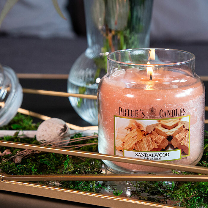 Zwei brennende Kerzen des Herstellers "Prices Candles" stehen nebeneinander auf einem rustikalen Holztisch. Die linke Kerze in einem Glasbehälter hat eine blaue Farbe und ist mit "Cotton Powder" beschriftet. Die rechte Kerze ist pink und trägt die Aufschr