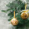 Zwei Weihnachtskugeln hängen an einem grünen Tannenbaum. Die linke Kugel ist schwarz und mit einem goldenen Weihnachtsbaum und Sonnenornamenten verziert. Die rechte Kugel ist goldfarben und trägt ebenfalls ein Sonnenornament. Beide Kugeln sind mit gelben 