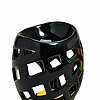 Ein dekorativer Teelichthalter aus glänzend schwarzer Keramik mit einem modernen, geometrischen Design. Die Oberfläche ist durchbrochen mit verschieden großen Rechtecken, die das Licht durchlassen. Innen sieht man ein sanftes, warmes Licht einer brennende
