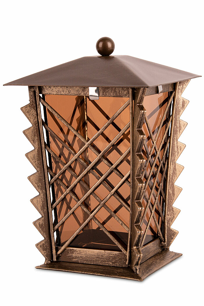 Eine bronzefarbene Laterne mit einem pyramidenförmigen Dach und einer dekorativen Kugel auf der Spitze. Die Seitenwände bestehen aus braunem, durchsichtigem Glas und sind mit einem markanten Zickzackmuster aus Metall verstärkt. Die Metallrahmen sind rusti