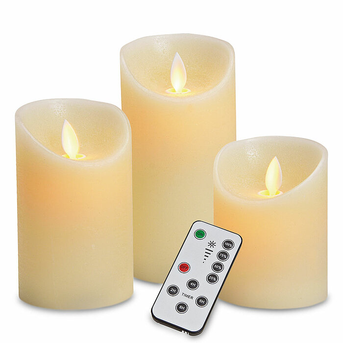 Drei cremefarbene, batteriebetriebene LED-Kerzen in verschiedenen Größen, mit flackernden Flammen. Vor den Kerzen liegt eine Fernbedienung mit verschiedenen Bedientasten für Timer und Flammeneffekte.
