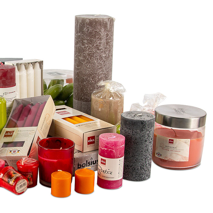 Mehrere verschiedene Kerzen in unterschiedlichen Formen, Größen und Farben. Darunter sind zwei orangefarbene Teelichter, mehrere rote und weiße Stabkerzen, pinkfarbene, graue und rote Stumpenkerzen sowie eine große runde Kerze in einem Glasbehälter. Es gi