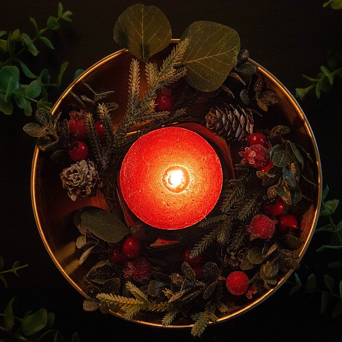 Goldene und silberne Weihnachtsdekorationen, darunter Kugeln, Sterne und eine Zapfen, liegen dekorativ auf einem mattschwarzen Hintergrund. Goldene und silberne Bänder schlängeln sich zwischen den Ornamenten und verleihen der Szene einen festlichen Glanz.