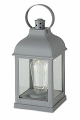 Eine graue Laterne mit einem metallischen Griff an der Oberseite. Die Laterne hat vier durchsichtige Glaswände, durch die man eine Kerze sehen kann, die von kleinen Lichterketten umgeben ist. Die Laterne steht auf einer hellen Oberfläche.