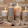 Vier brennende Kerzen aus natürlichem Wachs vom Hersteller "Wenzel" stehen auf einer hölzernen runden Platte. Die Kerzen tragen die Aufschrift "PURE NATURAL WAX" und sind in verschiedenen Größen angeordnet. Im Vordergrund liegen dekorative Holzstücke. Der