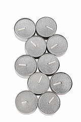 Neun silberne Teelichter, die dicht nebeneinander auf weißem Hintergrund angeordnet sind. Die Teelichter haben eine glänzende, leicht glitzernde Oberfläche und befinden sich in einem metallischen Gehäuse. Sie sind alle unangezündet und zeigen ihre Dochte 