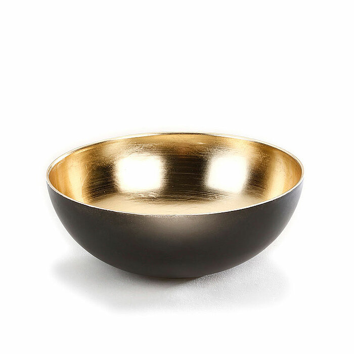 Eine stilvolle Schale mit einer glänzenden goldenen Innenseite und einer mattschwarzen Außenseite. Die Schale hat eine runde Form und steht auf einer weißen Oberfläche.