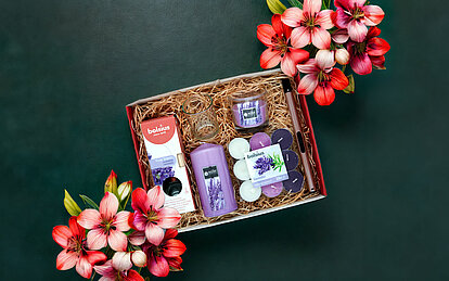 Blick von oben auf eine geöffnete Geschenkbox, die mit Stroh ausgelegt wurde. Darin wurden Produkte wie Duft-Stumpenkerzen, Duft-Teelichtern und Raumduft Diffuser gelegt.