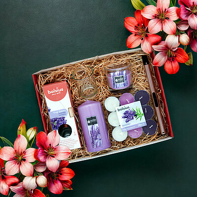 Blick von oben auf eine geöffnete Geschenkbox, die mit Stroh ausgelegt wurde. Darin wurden Produkte wie Duft-Stumpenkerzen, Duft-Teelichtern und Raumduft Diffuser gelegt.