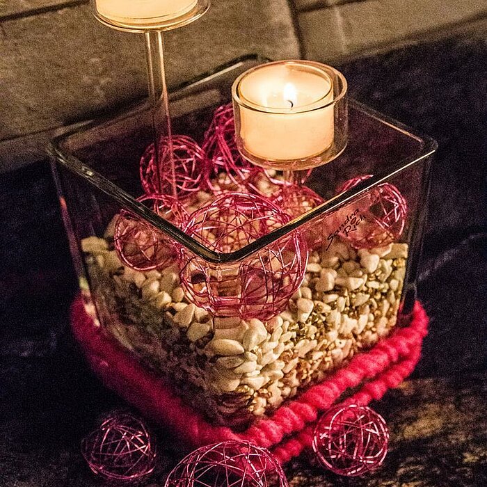 Zwei brennende Teelichter vom Hersteller "Sandra Rich" in transparenten Haltern, die in einem Glas mit Kaffeebohnen arrangiert sind. Eines der Teelichter steht erhöht auf einem stilvollen, klaren Ständer, während das andere direkt auf den Kaffeebohnen pla