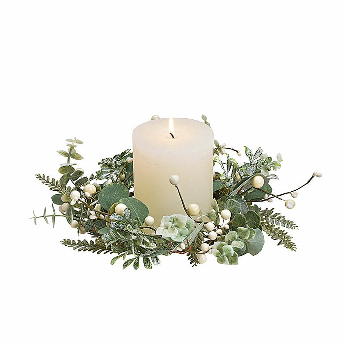 Eine einzelne brennende weiße Stumpenkerze ist in der Mitte eines grünen Kranzes aus künstlichen Blättern und Beeren platziert. Die Kerze und der Kranz stehen auf einer neutralen Oberfläche, und der Hintergrund ist weiß. Der Kranz besteht aus verschiedene