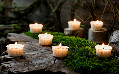 Ein moosbewachsener Stein mit vielen brennenden Papier-Teelichtern.