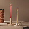 Zwei brennende Bolsius Tafelkerzen, eine rote und eine elfenbeinfarbene, in unterschiedlichen Kerzenhaltern auf einem runden Tisch. Auf dem Tisch befinden sich zudem eine beige und eine rote Stumpenkerze von Bolsius auf einem runden Tablett, sowie ein sch