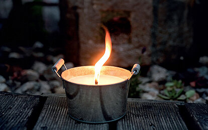 Nahaufnahme einer hell brennenden Zinkschale auf einer Terrasse.