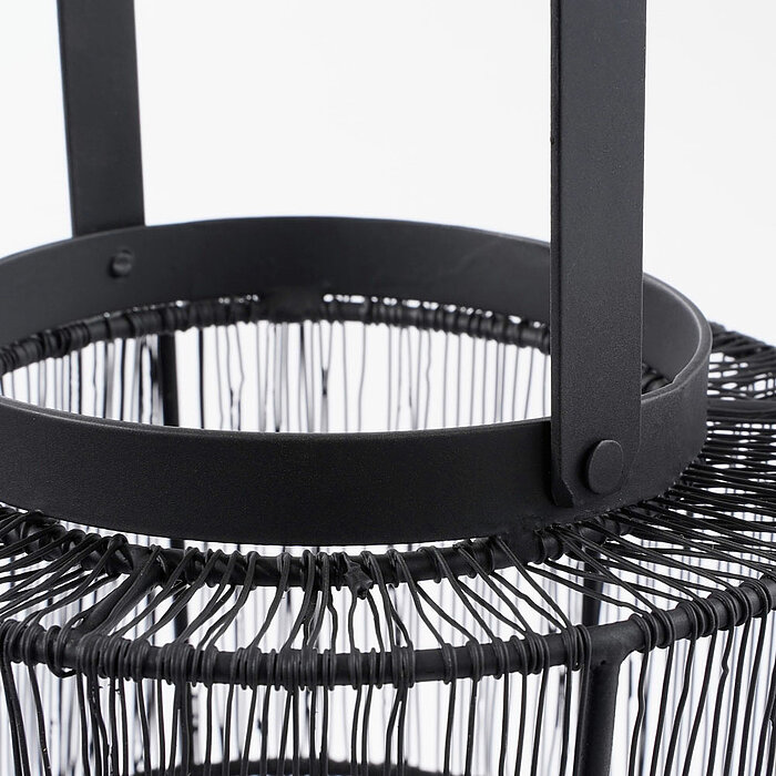 Schwarzes, metallisches und zylindrisches Objekt mit Drahtverflechtungen und einem Griff oben, das an einen modernen, minimalistischen Laternen- oder Körbchenstil erinnert. Das Design ist schlicht, funktional und stilvoll. Der Hintergrund ist schlicht und