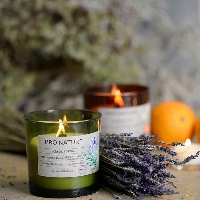 Die Abbildung zeigt ein Müller Pro Nature Raps-Duftglas (100/100 mm) mit dekorativem Holzdocht. Das Glas ist aus 100% recyceltem Material hergestellt und enthält natürliches Rapswachs, welches ca. 40 Stunden Brenndauer hat. Auf dem Glasetikett sind Illust
