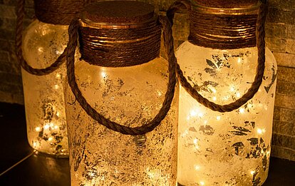 Nahaufnahme von drei LED Glasflaschen mit Korkdeckel und Sisal-Henkeln. Die Flaschen haben durch die gefrostete Oberfläche eine rustikale Oberfläche. Im Inneren leuchten LED Lichter und verbreiten ein warmes, gemütliches Licht.