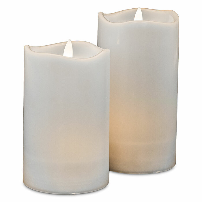 Zwei weiße, brennende LED-Kerzen verschiedener Größen. Die Kerzen haben eine realistische Flammenoptik und sind schlicht gestaltet. Sie stehen dicht nebeneinander auf einer neutralen, weißen Oberfläche, und die sanfte Beleuchtung erzeugt eine ruhige und e