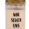 Eine weiße Gedenkkerze mit einem goldenen Deckel, auf der in schwarzen Buchstaben "WIR SEHEN UNS WIEDER!" geschrieben steht, wobei das Ausrufezeichen in rot hervorgehoben ist.