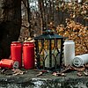 Sechs Kerzen (drei rote und drei weiße) von DecoLite, teilweise liegend, teilweise stehend, sind auf einer verfallenen Mauer in einem herbstlichen Wald ausgestellt. Eine schwarze Laterne von DecoLite steht in der Mitte, umgeben von trockenen Blättern. Im 