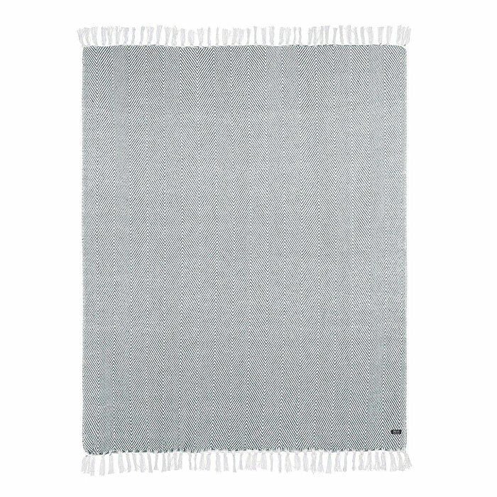 Ein stilvoll eingerichteter Raum mit grüner Wand. Im Mittelpunkt hängt ein Wandteppich mit der Abbildung einer botanischen Zeichnung. Rechts davon steht ein hoher schwarzer Metallregal mit verschiedenen Zimmerpflanzen in Körben sowie Kerzen und dekorative