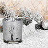 Ein Edelman Teelichthalter in Silber steht auf einer schneebedeckten Oberfläche. Der Halter ist mit einem winterlichen Baum- und Hirschmuster verziert. Im Hintergrund sind verschneite Zweige, Weihnachtskugeln und kleine, dekorative Tierfiguren zu sehen, d