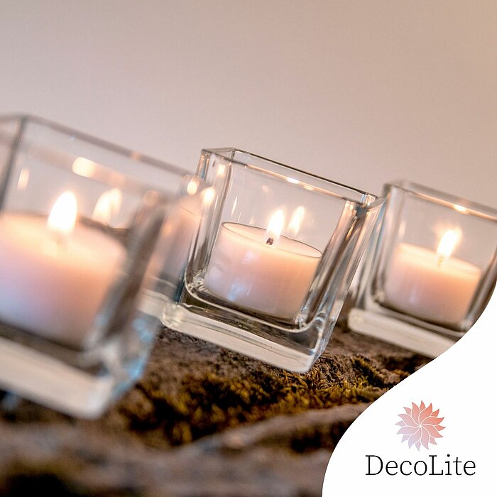 Auf dem Bild sind fünf verschiedene Nightlights von "DecoLite" zu sehen. Die Nightlights sind in Weiß und Transparentfarben gestaltet und brennen mit sanften Flammen. Die Kerzen sind auf verschiedenen Oberflächen platziert, darunter Holz und Glas, und erz