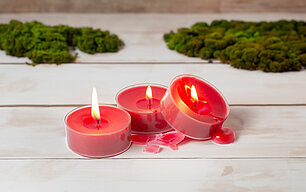 Nahaufnahme von brennenden Teelichtern, die schief auf einem Tisch stehen und daher auslaufen.