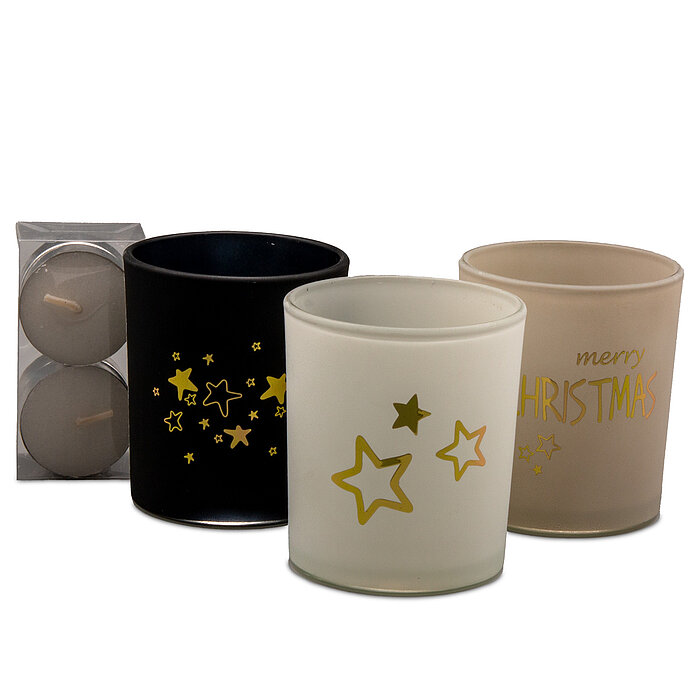 Vier Kerzen in dekorativen Gläsern stehen in einer Geschenkbox auf einer weißen Oberfläche. Die Gläser sind in den Farben Weiß, Grau und Schwarz gehalten und mit goldenen Sternen und Schriftzügen verziert. Im Hintergrund sind unscharfe, warme Weihnachtsli