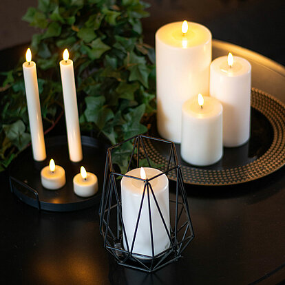 Ein eleganter schwarzer Tisch, dekoriert mit Efeu und verschiedenen LED-Kerzen, wie LED-Stumpen in verschiedenen Größen, LED-Teelichtern und LED-Stabkerzen.