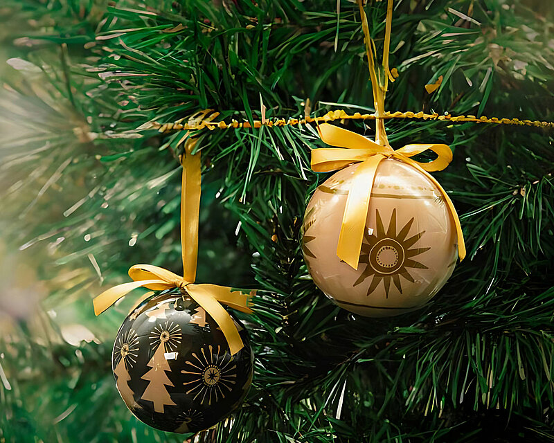 Zwei schöne Weihnachtskugeln mit zauberhaften Motiven schmücken einen festlichen, künstlichen Tannenbaum. Ihre glänzenden Oberflächen reflektieren warmes Licht und verbreiten eine einladende weihnachtliche Atmosphäre. Diese ausgewählte Dekoration symbolisiert die herzliche Tradition und die magische Stimmung, die die Weihnachtszeit mit sich bringt.