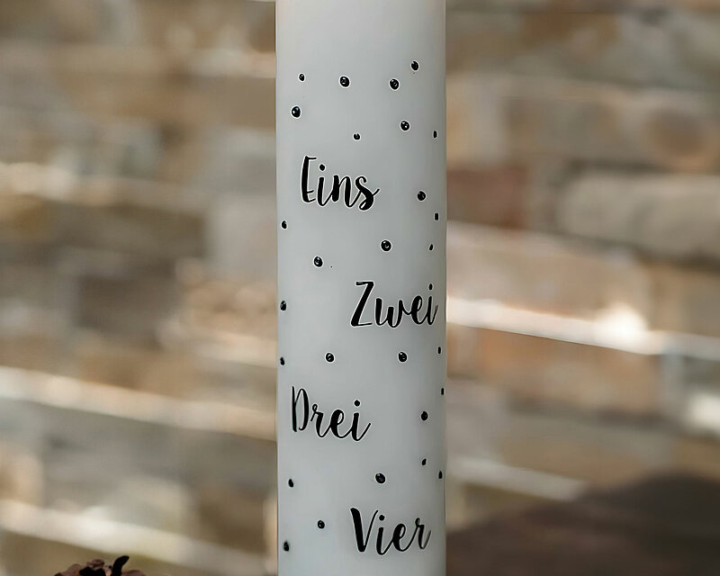 Eine weiße, brennende Adventskalenderkerze mit schwarzen Punkten und den Zahlen von eins bis vier steht auf einem liebevoll geschmückten Tisch. Umgeben von getrockneten Orangen, Walnüssen und Tannenzapfen verbreitet sie eine durch das Kerzenlicht eine warme und festliche Atmosphäre.