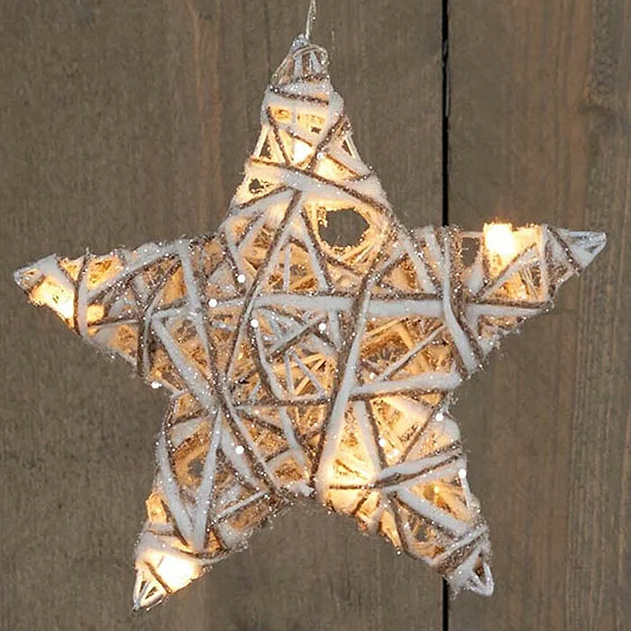 Eine sternförmige Dekoration, die aus gewebten, hellen Materialien gefertigt ist und mit kleinen Lichtern durchsetzt ist. Der Stern ist in Weiß- und Beigetönen gehalten und scheint sanft zu leuchten. Der Hintergrund besteht aus einer Holzoberfläche mit si
